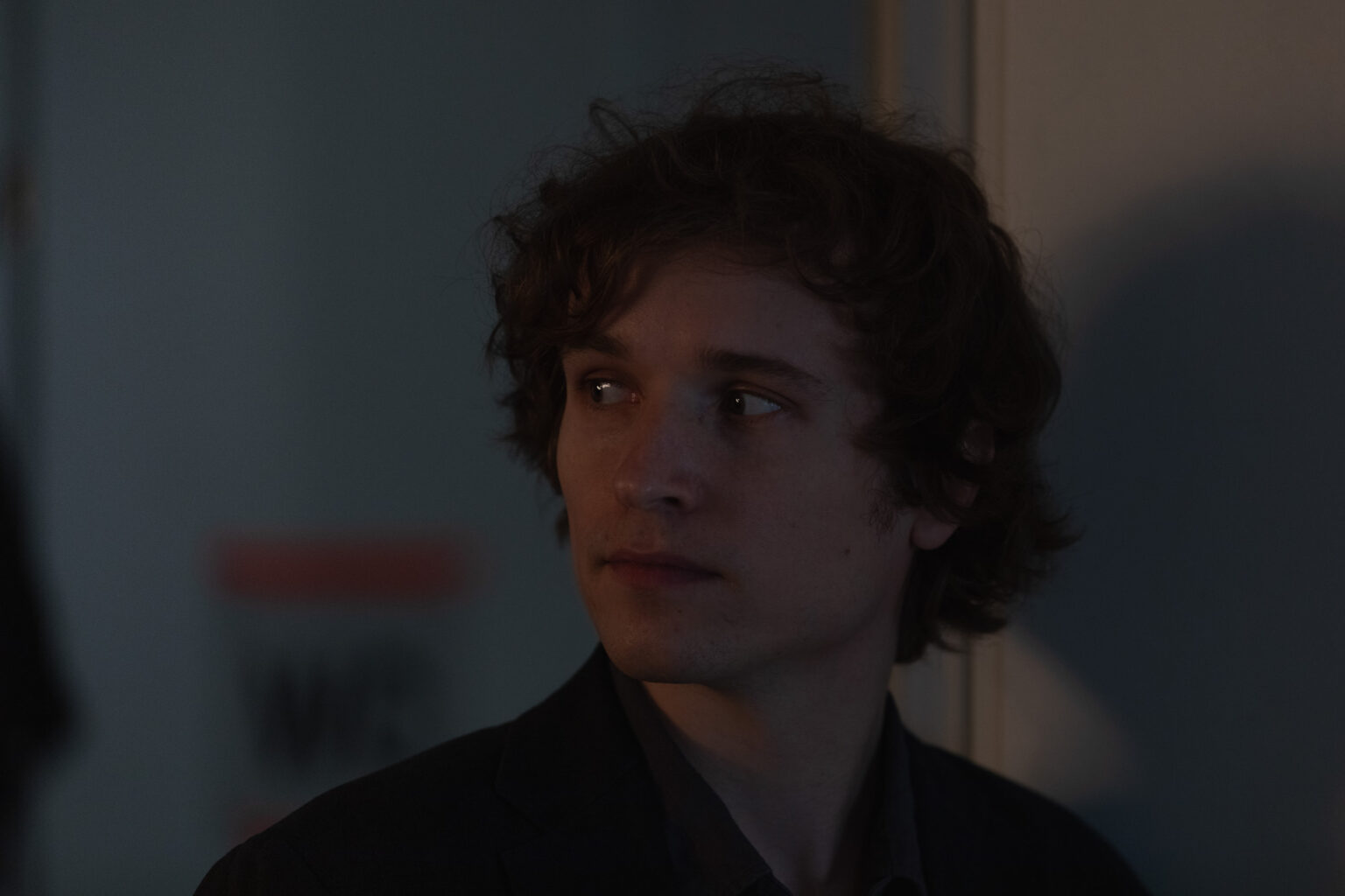 Porträt einer vermutlich männlichen Person. Die Person hat mittelkurze Locken und schaut konzentriert und interessiert nach links. Das Licht ist etwas schwummerig.